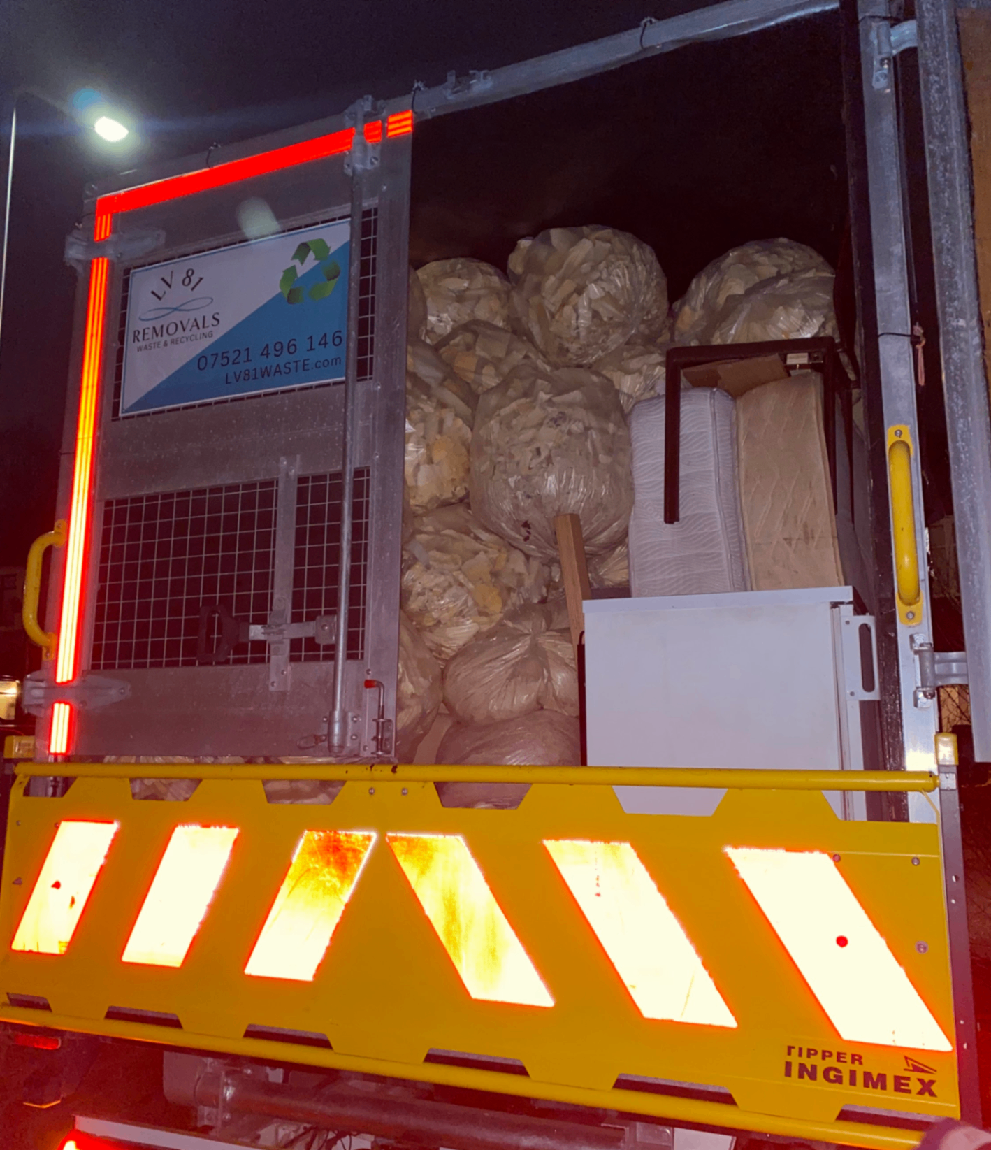 Night-time loaded truck packed with bagged waste and mattresses for removal